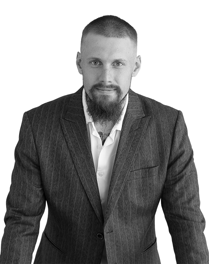 Роман Аносов - front-end web разработчик стоя у стола в полный рост смотрит в сторону зрителя